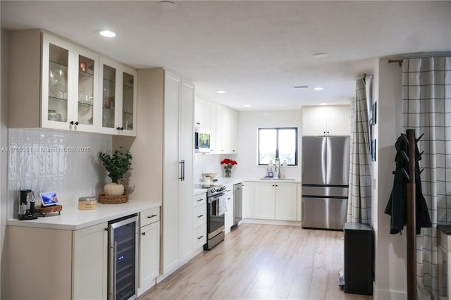 kitchen with beverage cooler, white cabinetry, light countertops, appliances with stainless steel finishes, and glass insert cabinets