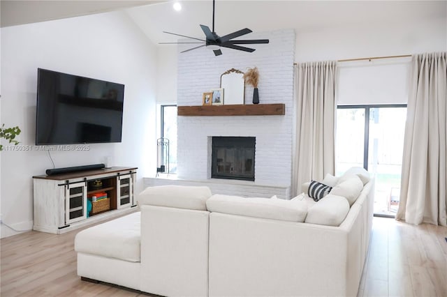 living area featuring light wood finished floors, a brick fireplace, vaulted ceiling, and a ceiling fan