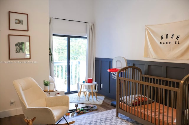 bedroom featuring a wainscoted wall, a decorative wall, and wood finished floors