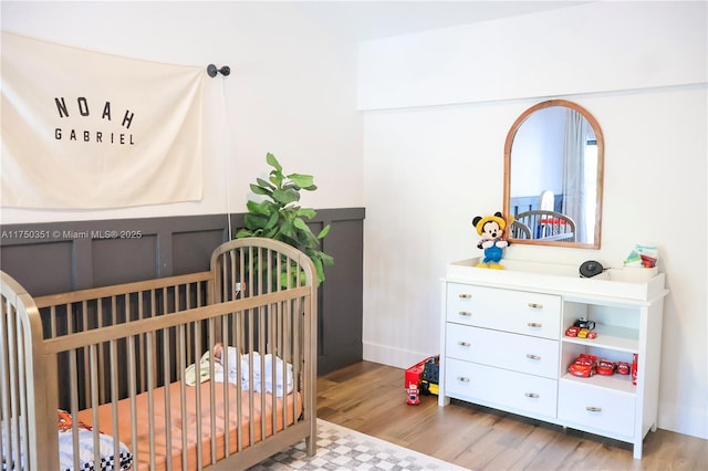 bedroom with a nursery area and wood finished floors