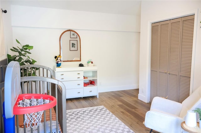 bedroom with a nursery area, a closet, baseboards, and light wood finished floors