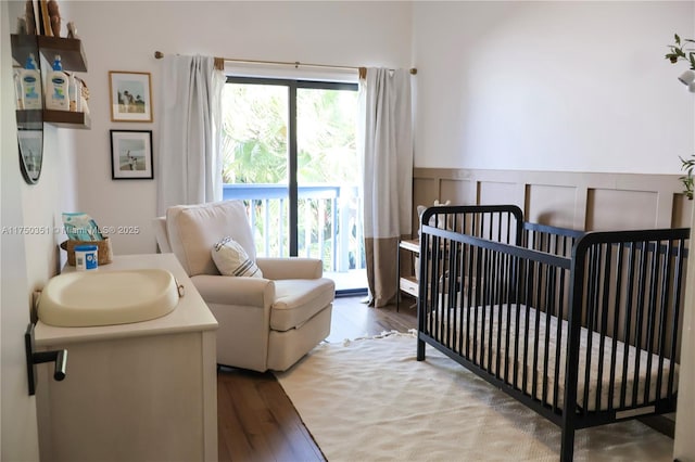 bedroom with a nursery area, wood finished floors, and a wainscoted wall