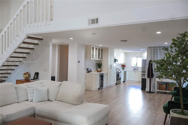 living area with recessed lighting, beverage cooler, visible vents, stairs, and light wood finished floors