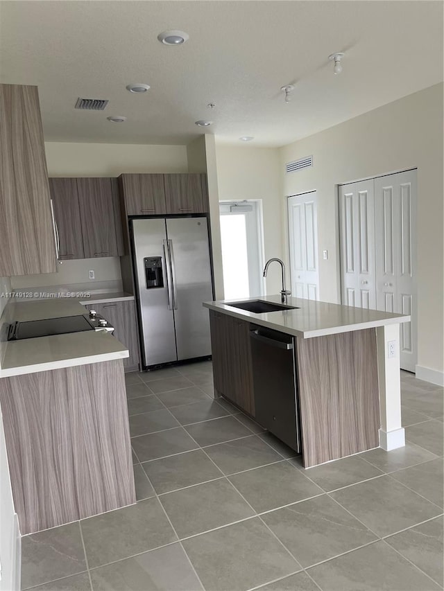 kitchen featuring dishwasher, light countertops, stainless steel refrigerator with ice dispenser, and a kitchen island with sink