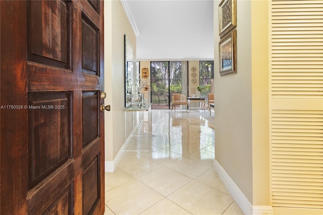 hallway with a wall of windows, light tile patterned flooring, crown molding, and baseboards