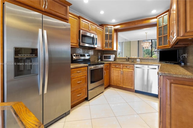 kitchen with light tile patterned floors, brown cabinetry, glass insert cabinets, appliances with stainless steel finishes, and a sink