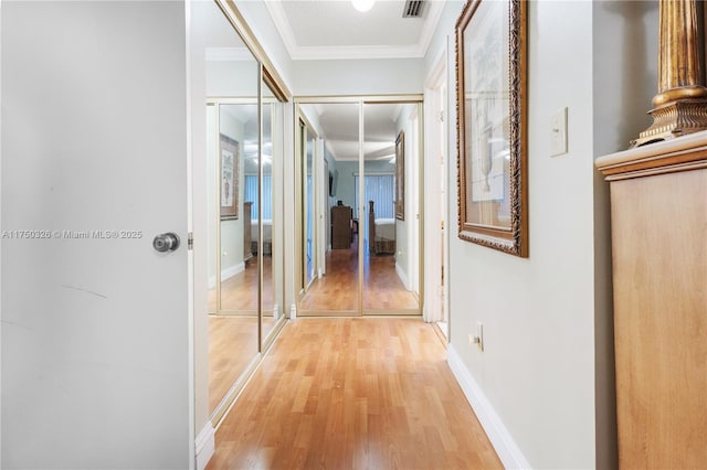 corridor featuring visible vents, crown molding, light wood-style flooring, and baseboards