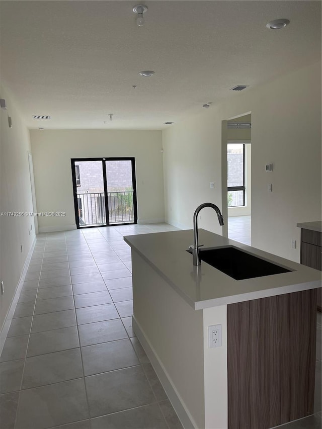 kitchen with light tile patterned flooring, a kitchen island with sink, a sink, open floor plan, and light countertops