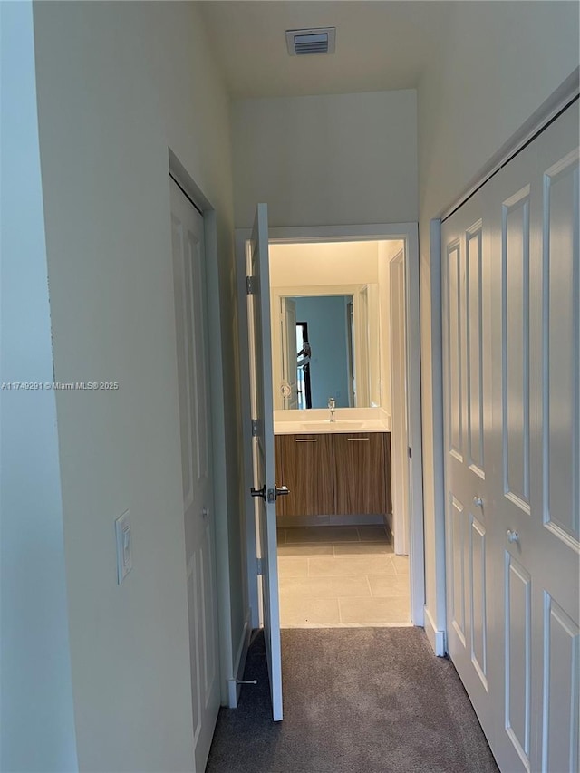 hallway with a sink, visible vents, and light colored carpet