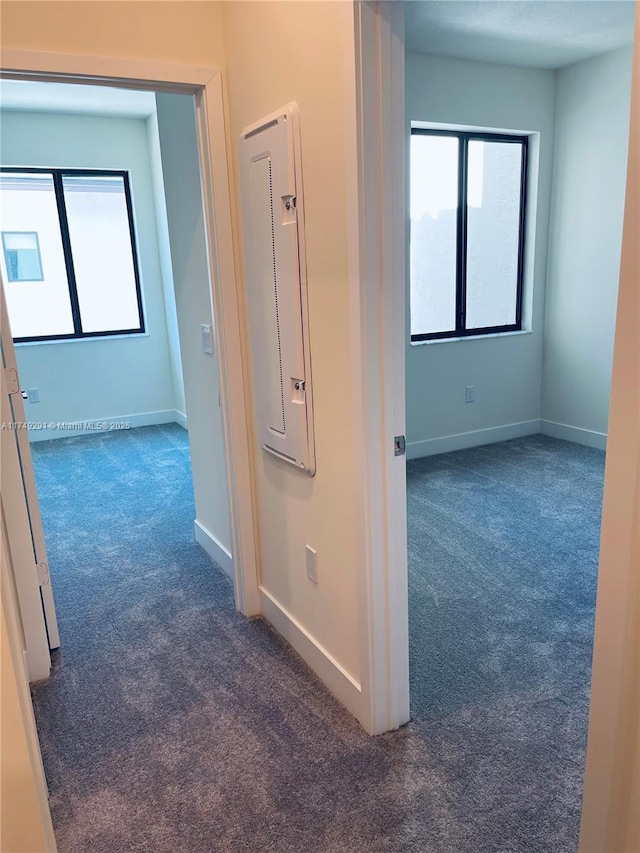 hallway with baseboards, electric panel, and dark carpet