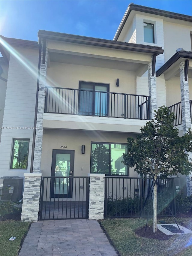 view of front of house featuring central AC, a gate, a balcony, and stucco siding