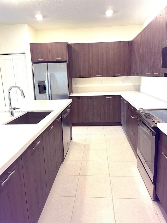 kitchen featuring light countertops, appliances with stainless steel finishes, light tile patterned flooring, a sink, and modern cabinets