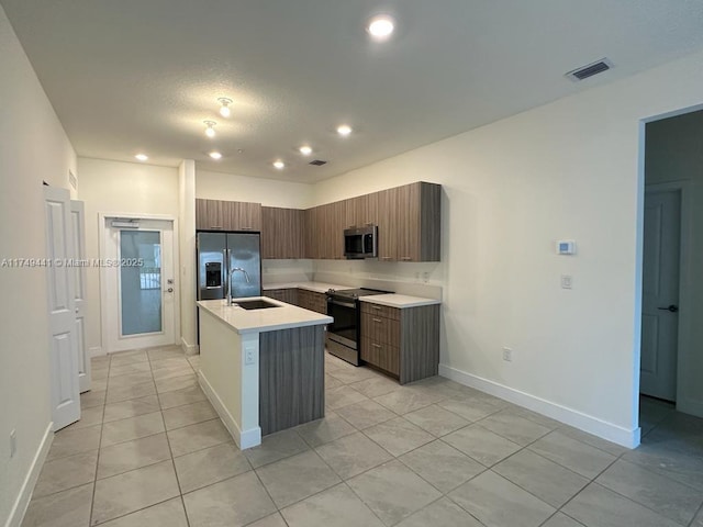 kitchen featuring stainless steel appliances, light countertops, a kitchen island with sink, a sink, and modern cabinets