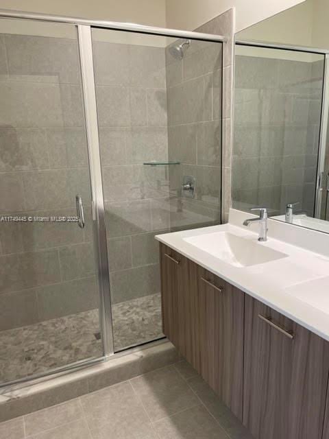 bathroom with double vanity, a sink, a shower stall, and tile patterned floors