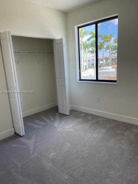 unfurnished bedroom with a closet, dark carpet, and baseboards