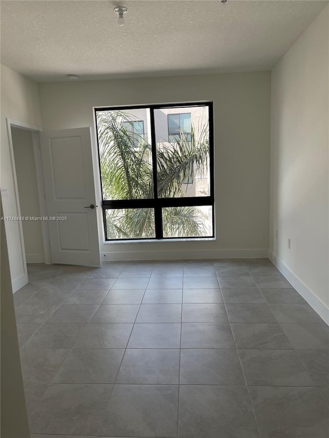 spare room with light tile patterned floors, baseboards, and a textured ceiling