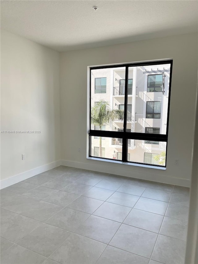 spare room with a textured ceiling, baseboards, and light tile patterned floors