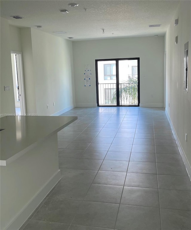 unfurnished room with visible vents, a textured ceiling, baseboards, and light tile patterned floors