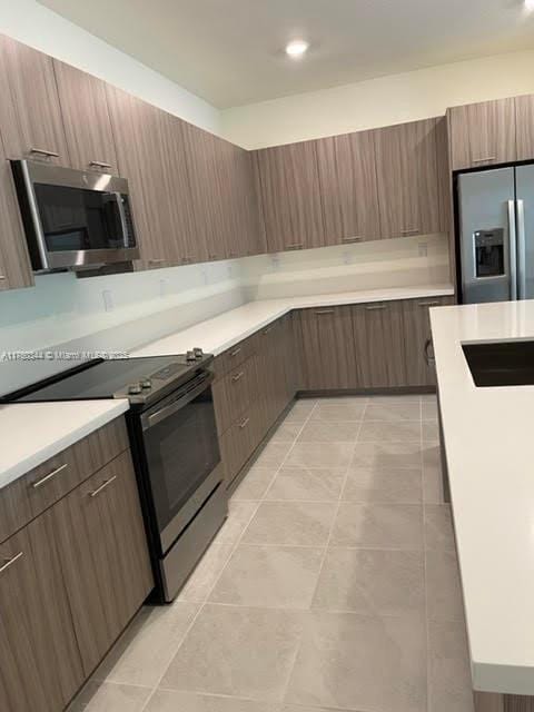 kitchen with light tile patterned floors, light countertops, appliances with stainless steel finishes, and modern cabinets