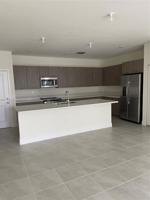 kitchen with stainless steel appliances, light countertops, a kitchen island with sink, a sink, and modern cabinets