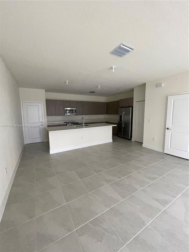 kitchen featuring a kitchen island with sink, dark brown cabinetry, visible vents, appliances with stainless steel finishes, and modern cabinets