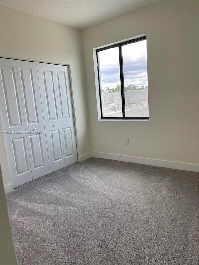 unfurnished bedroom featuring carpet floors, a textured ceiling, baseboards, and a closet