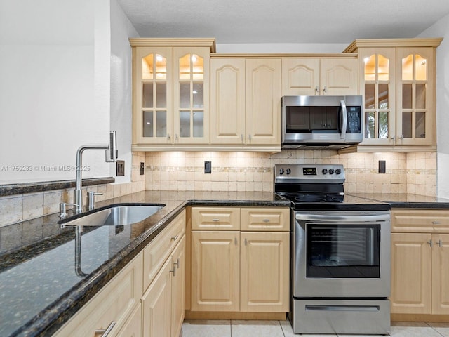 kitchen with dark stone counters, stainless steel appliances, a sink, and glass insert cabinets