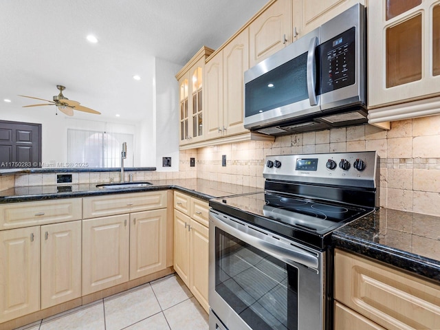 kitchen with dark countertops, glass insert cabinets, stainless steel appliances, and a sink