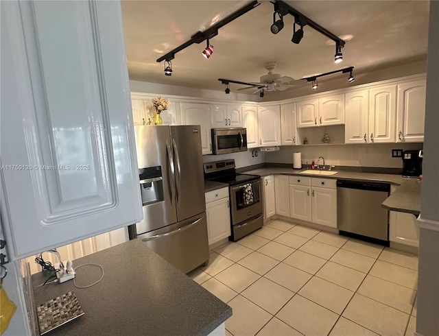 kitchen with stainless steel appliances, dark countertops, a sink, and white cabinetry