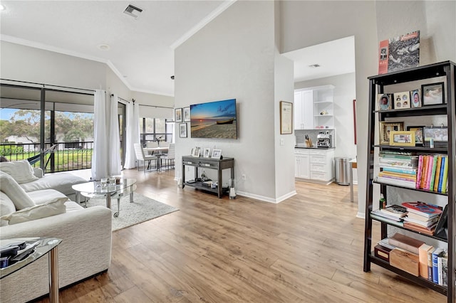 living area featuring light wood finished floors, baseboards, visible vents, ornamental molding, and a high ceiling