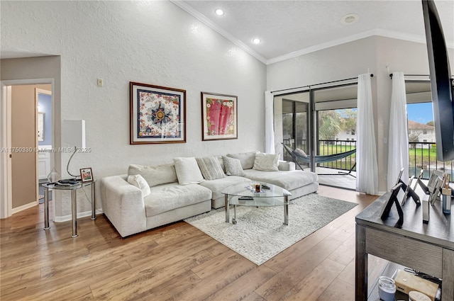 living room featuring lofted ceiling, a textured wall, light wood-style flooring, baseboards, and ornamental molding