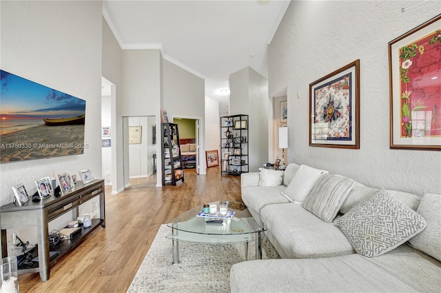 living room with crown molding, a textured wall, light wood-style flooring, a high ceiling, and baseboards