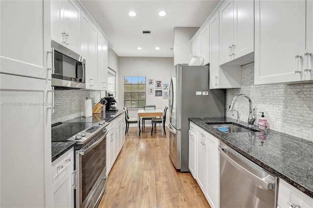 kitchen featuring white cabinetry, stainless steel appliances, a sink, and dark stone counters