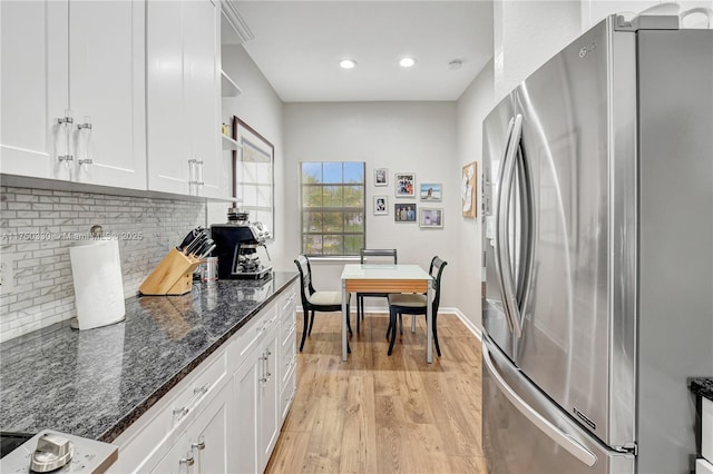 kitchen with backsplash, freestanding refrigerator, white cabinetry, dark stone countertops, and light wood-type flooring