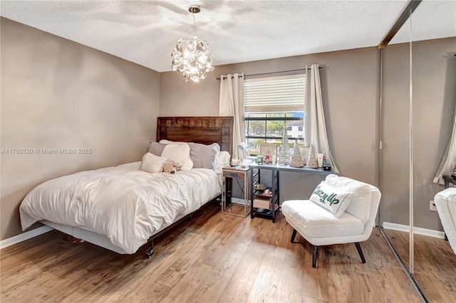 bedroom with a textured ceiling, a chandelier, wood finished floors, and baseboards