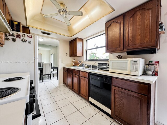 kitchen featuring white microwave, light countertops, dishwasher, a sink, and a raised ceiling