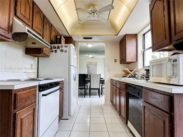kitchen featuring under cabinet range hood, a raised ceiling, a ceiling fan, visible vents, and white appliances