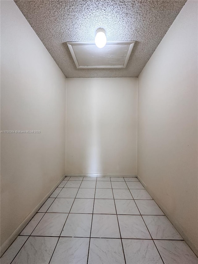unfurnished room with attic access, a textured ceiling, and light tile patterned floors