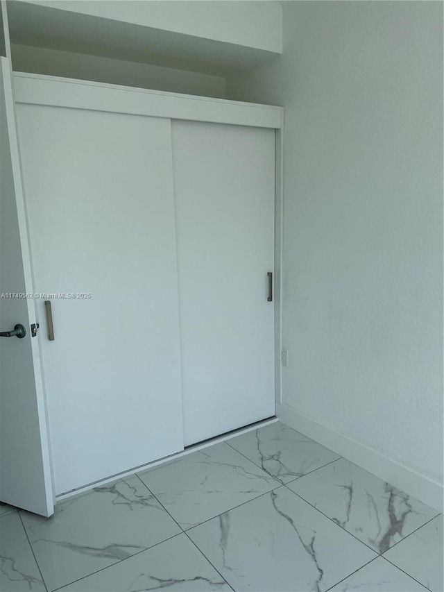 unfurnished bedroom with a closet, marble finish floor, and baseboards