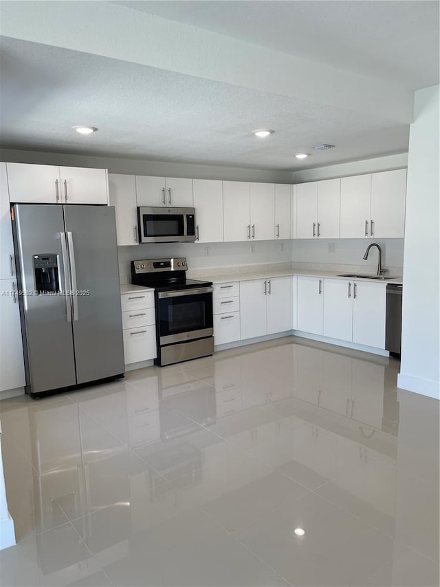 kitchen featuring light tile patterned floors, stainless steel appliances, a sink, white cabinetry, and light countertops