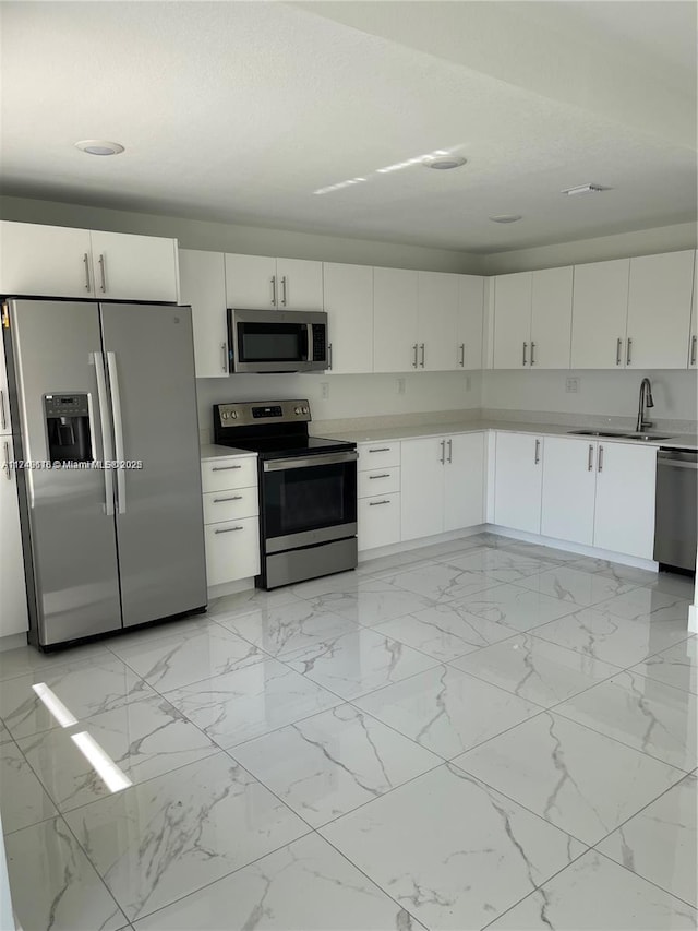 kitchen with appliances with stainless steel finishes, white cabinets, a sink, and light countertops