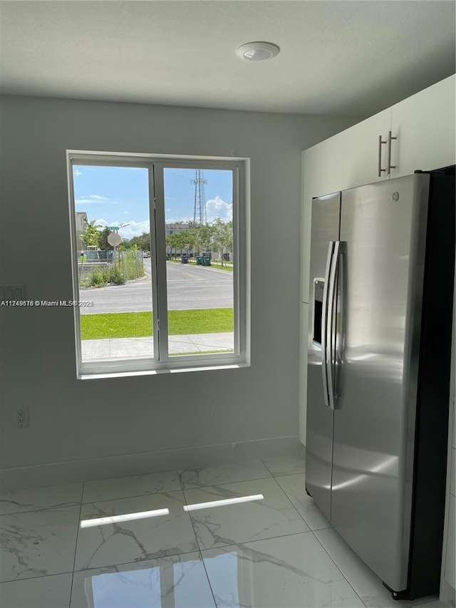 kitchen featuring marble finish floor, white cabinetry, stainless steel refrigerator with ice dispenser, and baseboards