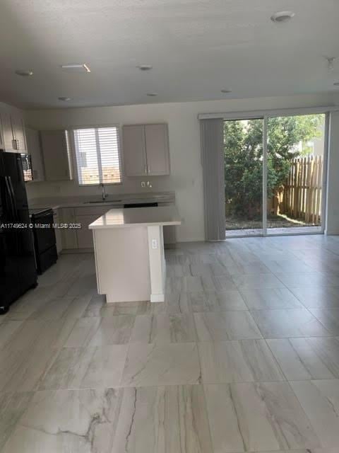 kitchen featuring light countertops, gray cabinetry, freestanding refrigerator, a kitchen island, and a sink