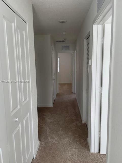 hall with visible vents and light colored carpet