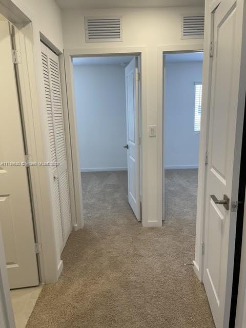 hall featuring light carpet, visible vents, and baseboards