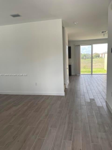 spare room with visible vents, baseboards, and dark wood-type flooring