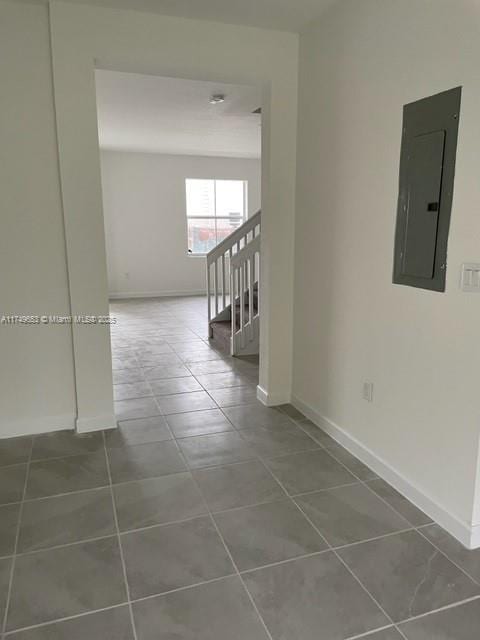 corridor with stairs, dark tile patterned flooring, electric panel, and baseboards