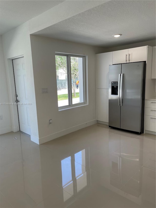 kitchen with light tile patterned floors, a textured ceiling, white cabinetry, baseboards, and stainless steel refrigerator with ice dispenser