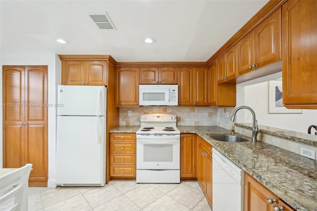 kitchen with a sink, white appliances, and light stone counters