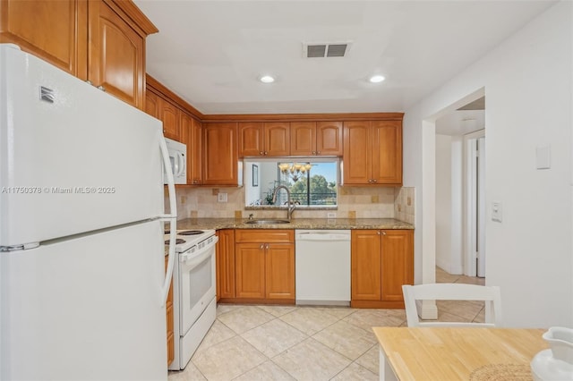 kitchen with white appliances, brown cabinetry, a sink, and light stone countertops